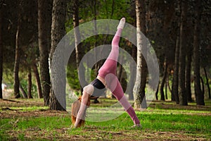 Redhead young woman doing one legged downward facing dog yoga pose in a forest.