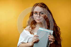 Redhead young woman holding blank books looking at the camera isolated yellow