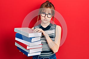 Redhead young woman holding a pile of books depressed and worry for distress, crying angry and afraid