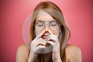 Redhead young woman pinching her nose over pink background.