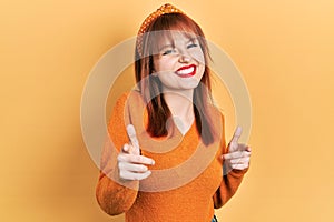 Redhead young woman wearing casual orange sweater pointing fingers to camera with happy and funny face