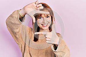 Redhead young woman wearing casual winter sweater smiling making frame with hands and fingers with happy face