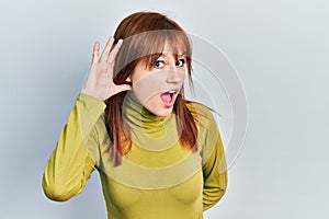 Redhead young woman wearing turtleneck sweater smiling with hand over ear listening and hearing to rumor or gossip