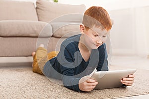 Redheaded boy playing on digital tablet on carpet