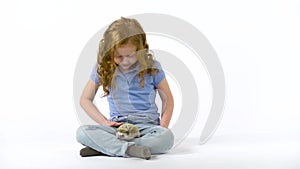 Redheaded little girl with curly hair is holding hedgehog at white background. Slow motion