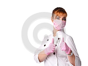 Redheaded woman, nurse or doctor, in medical suit, pink mask and disposable gloves. Showing thumbs up, posing isolated on white