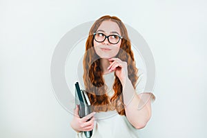 Redheaded woman student in eyeglasses with books in her hand looks thoughtful standing on  white backgroung, learning and