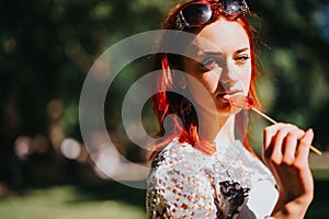 Redheaded young girl enjoying a sunny day in the park with a lollipop