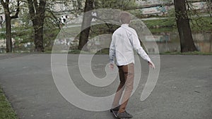 Redheaded young man with a beard foots starts ride on longboard in sunset park.