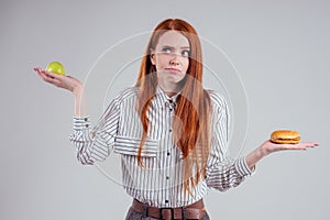 Redheared hungry business woman in striped shirt eating USA burger visa traveler white background studio choosing
