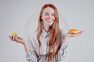 Redheared hungry business woman in striped shirt eating USA burger visa traveler white background studio choosing