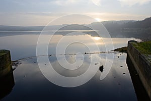 Redmires reservoir dam inlet overflow reflecting a misty water sunset