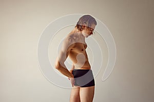 Reduction of back pains. Shirtless young guy with healthy, fit, muscular body standing in underwear against grey studio