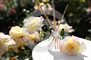 Reed air freshener with oil and fresh rose on table against blurred background