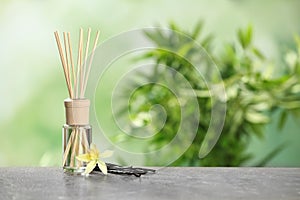 Reed air freshener with vanilla flower and sticks on grey table against blurred green background