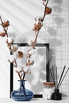 Reed diffuser, candle and cotton branches with fluffy flowers on white wooden table indoors