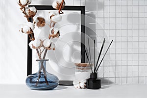 Reed diffuser, candle and cotton branches with fluffy flowers on white wooden table indoors. Space for text