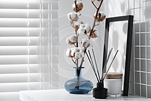 Reed diffuser, candle and cotton branches with fluffy flowers on white wooden table indoors. Space for text