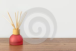 Reed diffuser with scented oil bamboo sticks in red glass bottle on wooden table white wall background. Aromatherapy home interior