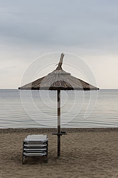 Reed Parasol With Sun Loungers on Sandy Beach. Umbrella and Sunbeds on Gloomy Weather and Calm Sea. Reed Umbrella and Easy