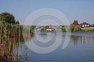 Reeds along banks of river with river houses docked on the opposite side reflecting in still waters. Fishing lake photo