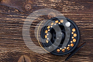 Reel with orange fishing line for fishing rod lies on a dark wooden background