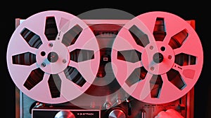 Reel to reel tape recorder illuminated by red light. Close up of vintage music player with two round metallic bobbins