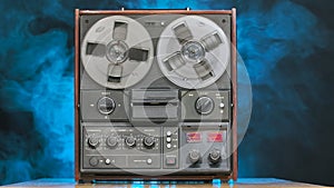 Reel to reel tape recorder playing against a smoky studio background with blue neon lights. Rotating vintage music