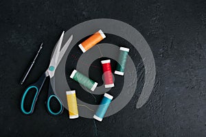 Reels of thread scattered on the table, tailors scissors and thread cutter, dark background