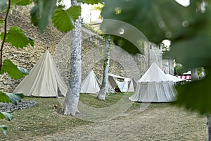 Reenactment of a medieval scene against the historical backdrop of an old city wall, village with tents of various designs with