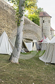 Reenactment of a medieval scene against the historical backdrop of an old city wall, village with tents of various designs with