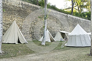 Reenactment of a medieval scene against the historical backdrop of an old city wall, village with tents of various designs with