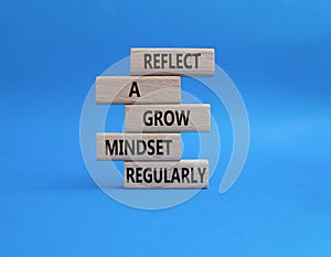 Refclect a grow mindset regularly symbol. Wooden blocks with words Refclect a grow mindset regularly. Beautiful blue background.