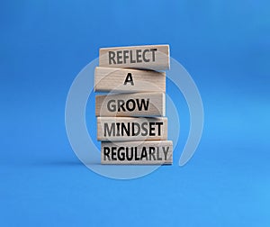 Refclect a grow mindset regularly symbol. Wooden blocks with words Refclect a grow mindset regularly. Beautiful blue background.