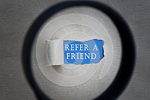Refer A Friend text on torn paper with magnifying glass. Network concept.