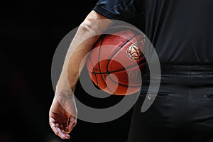 A referee with black uniform holds the official basket game ball