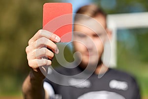 Referee hands with red card on football field