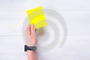 The referee`s hand holds a penalty yellow card, on a gray background