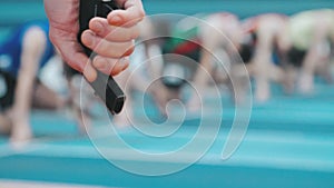 Referee`s hand with starting pistol on blurred background of athletes