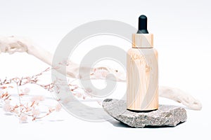 Refillable bamboo dropper bottle with organic cosmetic liquid, herbal oil or face serum against white background