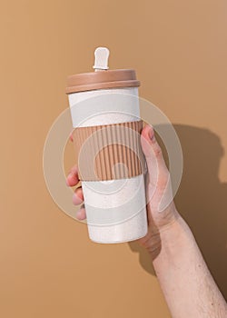 Refillable cup in young mans hand on beige background. Concept of plastic-free and zero waste living
