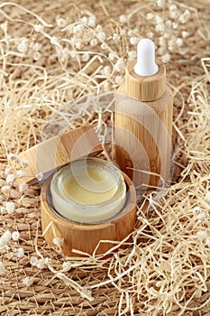 Refillable glass dropper bottle and open cream or salve jar covered bamboo wood