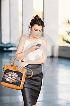 Refined smiling woman walking and writing or reading SMS messages online on a smart phone outdors