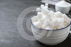 Refined sugar cubes in bowl on grey table. Space for text