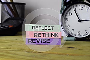 Reflect Rethink Revise. Handwriting on sticky notes in clothes pegs on wooden office desk