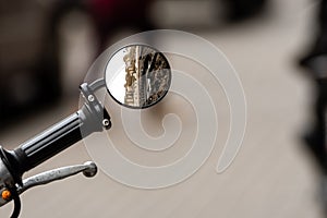 Reflection of a ancient residental building in the rear view mirror of a motorcycle in front of a blurred sidewalk