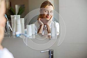 Reflection of attractive Caucasian blonde woman in mirror with perfect skin. Skincare.