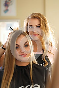 Reflection of beautiful blonde female hairdresser holding hair l