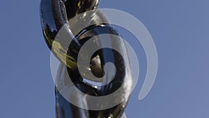 Reflection in black chain on background blue sky. Action. Close-up of black chain with reflection of greenery and sun