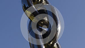 Reflection in black chain on background blue sky. Action. Close-up of black chain with reflection of greenery and sun